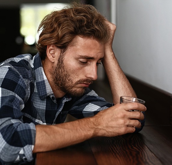 An unhappy man looking down at a glass of alcohol