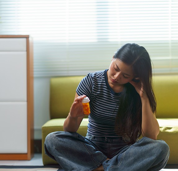 A woman sitting on the floor and holding a bottle of opioids