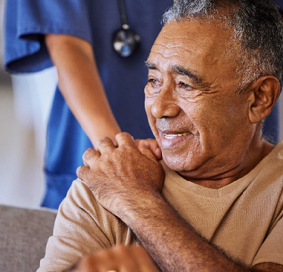 A nurse giving an older man support during his recovery