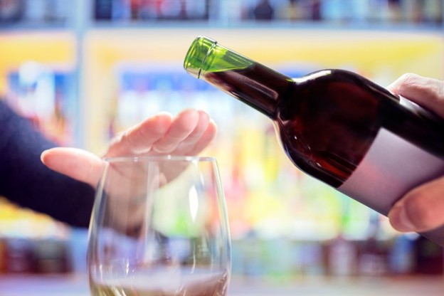A woman’s hand rejecting more alcohol from a wine bottle