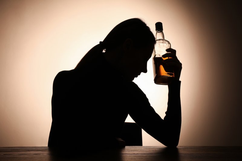 A shadowed woman sitting with a bottle of whiskey at a table